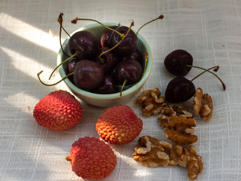 Ripe dark sweet cherries, Prunus avium, fresh lychee, Litchi chinensis, and walnut kernels, Juglans regia, arranged on natural linen. Seasonal fruit and nut composition suitable for healthy eating, nu
