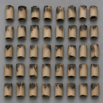 Overhead flat lay of collected spent firework casings arranged in an even grid on a plain grey surface, flat even light, honest documentary look