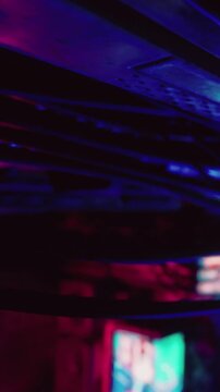 Bright lights and reflections illuminate a bustling urban scene at night. Neon signs and vibrant colors capture the energy of the city as people move around.