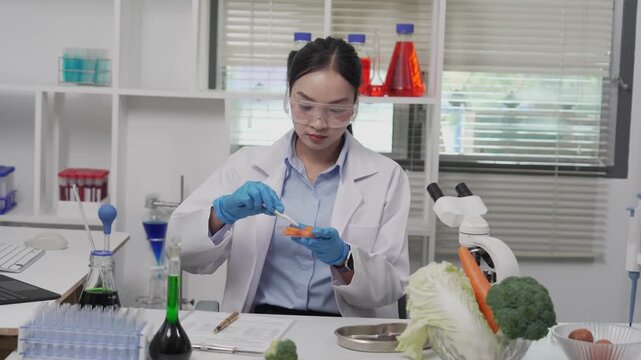 An Asian female food scientist wearing safety glasses and gloves holds fresh broccoli and carrots, inspecting their quality for pesticide residues or chemical contaminants in a food research laborator