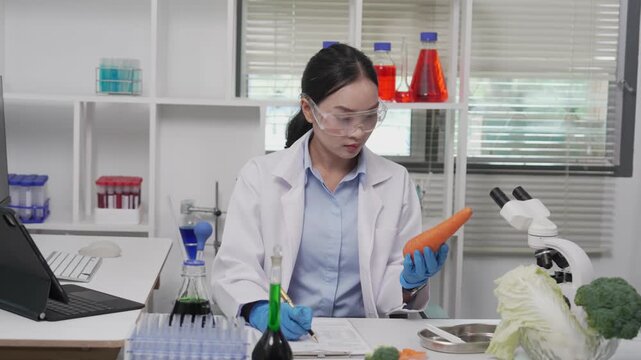 An Asian female food scientist wearing safety glasses and gloves holds fresh broccoli and carrots, inspecting their quality for pesticide residues or chemical contaminants in a food research laborator