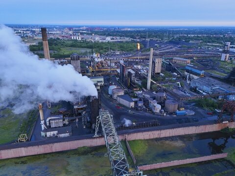 River Rouge, Michigan, United States - 08 August 2026: Aerial view of Zug Island industrial complex with smoking chimneys, storage tanks, and heavy machinery under a clear sky.