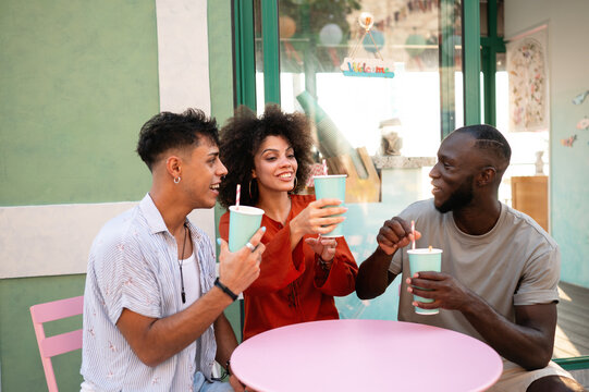 Diverse young friends enjoying contemporary cafe culture, laughing, toasting outside on a summer day