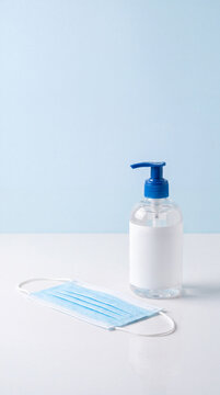 Hand sanitizer and a medical mask placed on a clean surface with a soft blue background