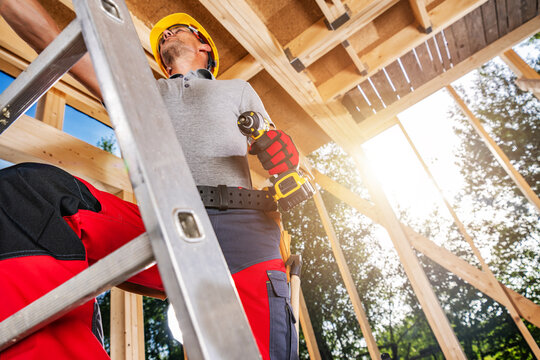 Worker using a drill while on a ladder in a building under construction