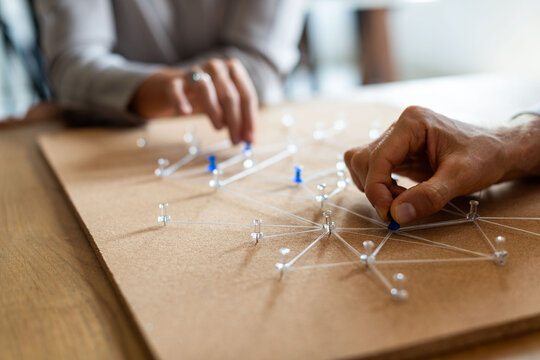 Hands arranging pins and strings on a corkboard, planning concept.