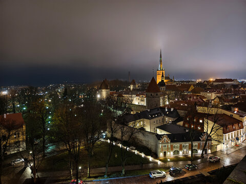 High angle wide view of illuminated Tallinn Old Town skyline at night with medieval city wall towers and St. Olaf's Church spire in Estonia