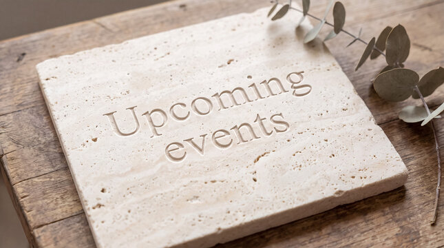 Upcoming events message engraved on a natural stone tablet resting on an old wooden table with dried eucalyptus
