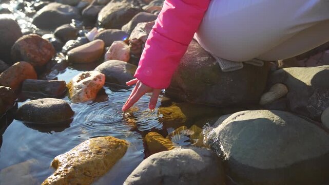 Ripples child water touching calm pond surface on rocky shore during sunny autumn day for peaceful nature exploration