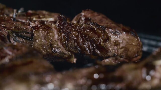 Close up of juicy seasoned steak sizzling on grill with rosemary and char marks