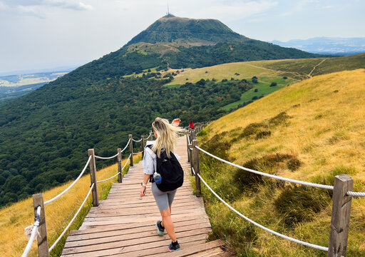 woman hiking on wooden boardwalk in green forest with roped railings, first person perspective from behind her, adventure mood, mountain trail setting, brown and green colors, natural light.