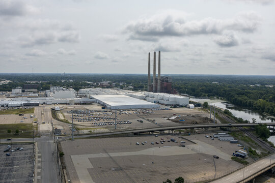 Lansing, United States - 10 August 2026: Aerial view of Amazon Fulfillment Center IMI1 featuring large warehouse buildings, expansive parking lots, and a nearby power plant with three smokestacks.