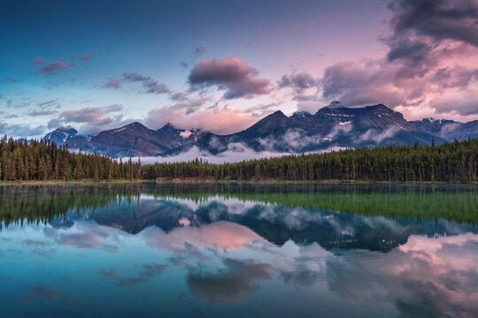 Symmetrical mountain reflection at Herbert Lake during purple sunset in Banff Canada