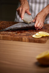 Chef hands scaling fresh fish on cutting board © Rychko Yevhen
