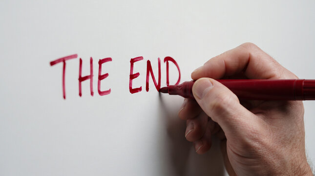 Mano pintando con spray rojo las palabras &laquo;THE END&raquo; sobre una pared blanca, simbolizando el final o la conclusi&oacute;n de una etapa.