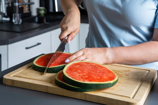 Woman cutting thick watermelon slices into smaller pieces on a wooden cutting board