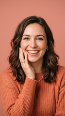 Fototapeta premium Cheerful young woman with wavy brown hair posing happily while wearing a cozy ribbed sweater against a soft terracotta background