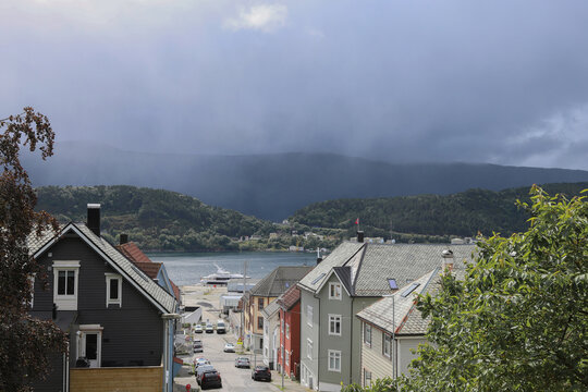 Norwegian Coastal Street View in Alesund. Traditional scandinavian coastal houses with ocean bay, mountains under dramatic sky, Norway.