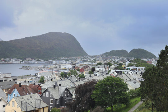 Traditional coastal houses and harbor in Alesund town, Norway. Scandinavian cityscape with ocean bay, mountains under dramatic sky.
