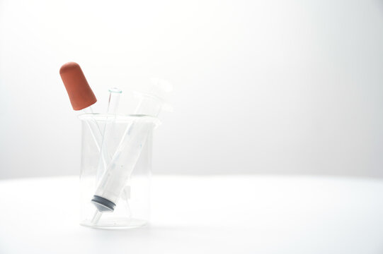 Medical syringe and vial arranged inside clear beaker against bright white background, creating clean clinical concept for healthcare, laboratory research, injection, and pharmaceutical