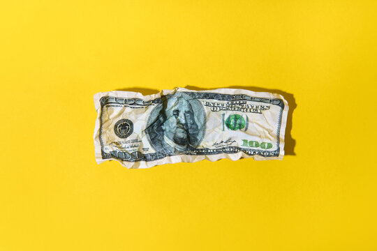 Crumpled hundred dollar bill on yellow background