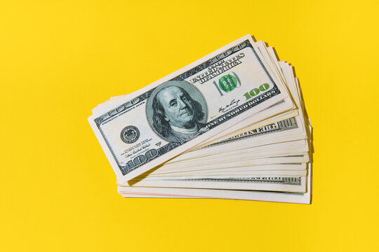 Stack of hundred dollar bills on bright yellow background