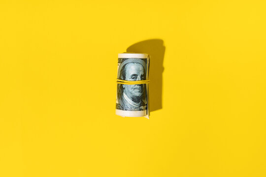 Roll of hundred dollar bills on yellow background