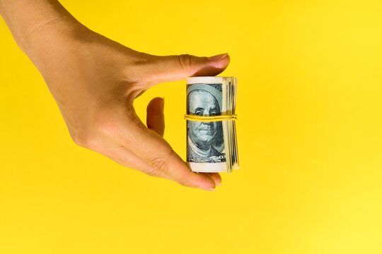  Hand holding roll of hundred dollar bills