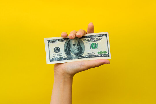 Hand holding hundred dollar bills on yellow background