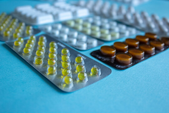Blister packs of medical pills on blue background close up, perspective view of assorted pharmaceutical tablets and gelatin capsules in foil packaging, healthcare and drugstore concept