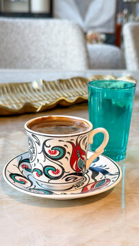 Traditional Turkish coffee in a colorful ceramic cup with a glass of water on a marble table, cozy coffee break and cultural beverage concept.