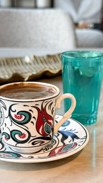 Traditional Turkish coffee in a colorful ceramic cup with a glass of water on a marble table, cozy coffee break and cultural beverage concept.