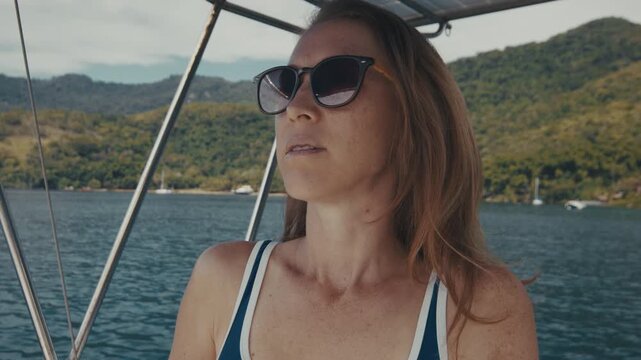 Young woman in sunglasses sits in the cockpit of the sailing boat near the helm and looks around