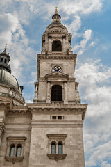 Naklejka premium Bell tower with a clock face rising beside the dome of Saint Stephen's Basilica in Budapest, Hungary