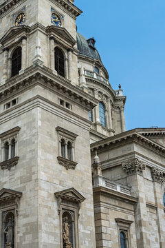 Corner facade view of the clock tower and dome base of Saint Stephen's Basilica against a blue sky in Budapest