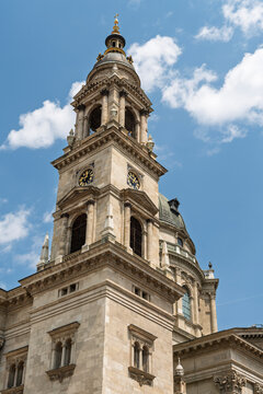 Full view of the clock tower and copper dome of Saint Stephen's Basilica against a partly clouded sky in Budapest