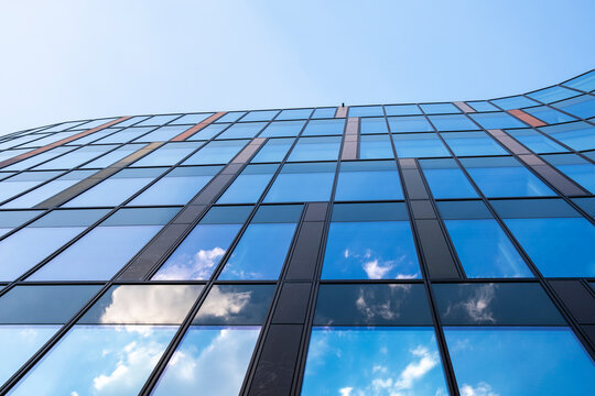 A modern building shows reflection in glass facade and windows, where blue sky and clouds sharpen the geometry of the architecture
