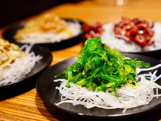 A small plate of bright green chuka wakame seaweed appetizer presented on a wooden table alongside other Japanese side dishes © Imageswin