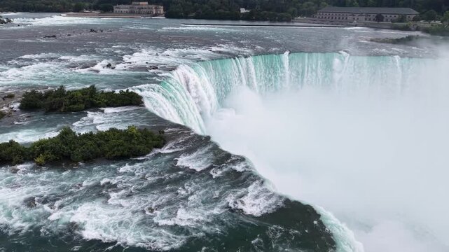 High-angle aerial shot circling the iconic curved green water crest, rocky islets, and heavy rising mist of the Horseshoe Falls on the Niagara River in Ontario, Canada