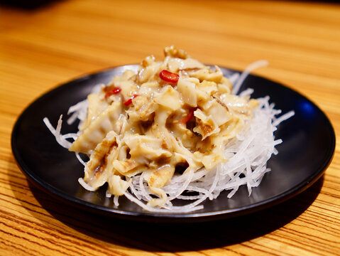 Close-up shot of Japanese chuka hotate seasoned scallop skirt salad garnished with red chili on shredded daikon radish in a black plate