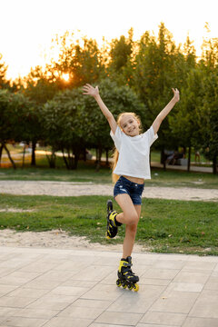 A joyful girl poses in the park on one roller skate with her arms raised