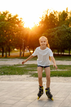 A lovely fair-haired girl is skating on yellow roller skates in the golden hour sunlight