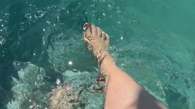 A pair of bare feet wading in crystal clear turquoise tropical ocean water, suggesting relaxation and vacation moments, perfect for travel content