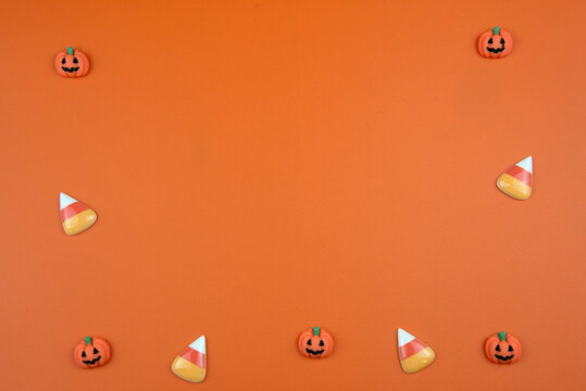 Halloween candy pumpkins and traditional candy corn creating a festive border on a vibrant orange background, ideal for seasonal design