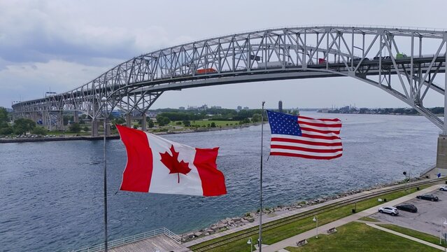Port Huron, United States - 27 July 2026: Aerial view of the Blue Water Bridge spanning the St. Clair River with Canadian and American flags flying in the foreground.