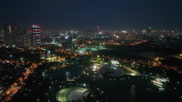 Panoramic aerial view of Hoa Binh Peace Park and the illuminated Hanoi cityscape at night, featuring lakes, roads, buildings, and urban lights.