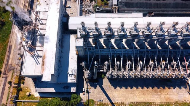 Overhead aerial view of industrial plant processing towers and pipes. Rows of metal processing vessels and connected pipes create geometric shadows on concrete ground.