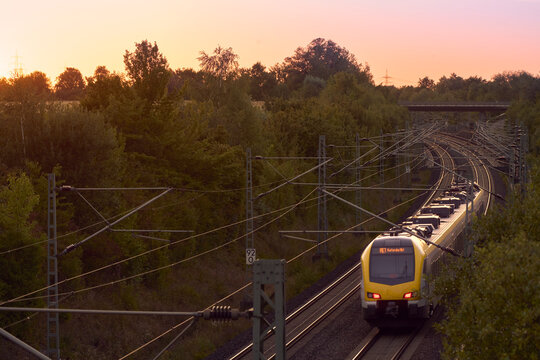 Intercity train traveling through a scenic railway corridor at sunset, surrounded by trees and overhead power lines. Stuttgart to Mannheim, Baden-W&uuml;rttemberg, Germany