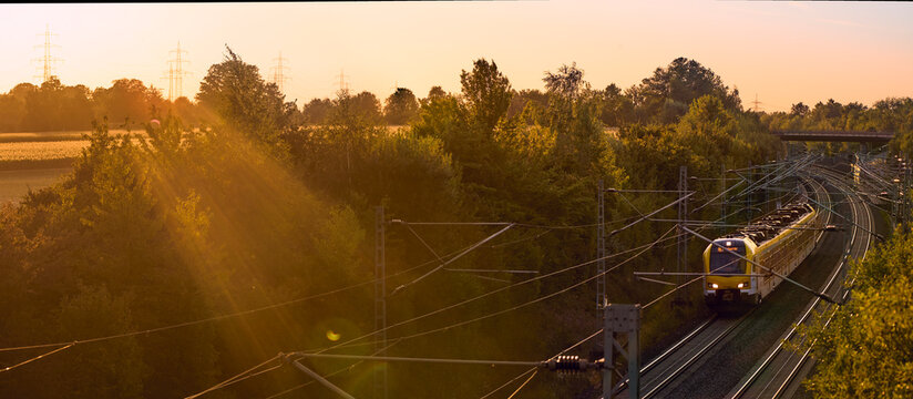 Intercity train traveling through a scenic railway corridor at sunset, surrounded by trees and overhead power lines. Stuttgart to Mannheim, Baden-W&uuml;rttemberg, Germany