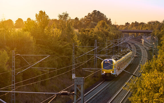 Intercity train traveling through a scenic railway corridor at sunset, surrounded by trees and overhead power lines. Stuttgart to Mannheim, Baden-W&uuml;rttemberg, Germany